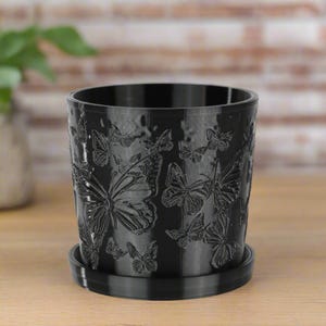 May include: A black plastic planter with a raised butterfly design. The planter has a matching saucer.