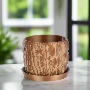 May include: A bronze-colored, textured planter pot with a matching saucer. The pot has a rounded shape with a pattern of raised, irregular circles. The planter is designed for indoor or outdoor use.