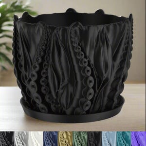 May include: Black decorative plant pot with a matching saucer. The pot features an intricate design of flowing, tentacle-like patterns around the exterior. The pot is made of a matte black material and is designed to hold plants.