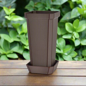 May include: A brown plastic planter with a matching saucer. The planter has a square top and a rounded bottom. The planter is sitting on a wooden surface.