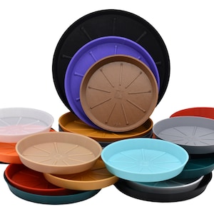 May include: A collection of colorful plastic plant saucers in various sizes. The saucers are in shades of black, purple, brown, yellow, orange, white, gray, red, teal, and blue. Each saucer has a raised center with radial lines.