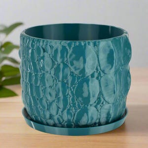 May include: Teal plastic planter with a textured, bubble-like design. The planter has a matching saucer.