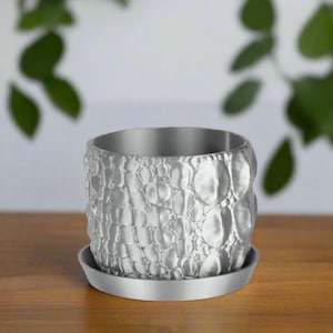 May include: A silver planter with a textured, bubble-like design. The planter has a matching saucer.