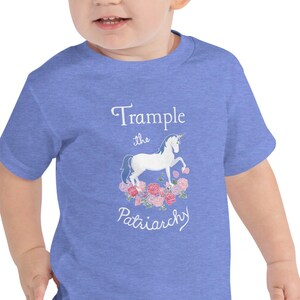 May include: A toddler wearing a blue short-sleeved t-shirt with a white unicorn graphic and the text "Trample the Patriarchy".