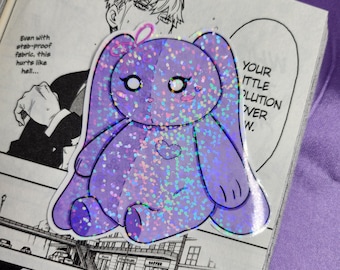 May include: A sparkly purple bunny sticker with a pink bow and glitter. The sticker is on a page of a manga comic book with text that reads "Your little revolution over."