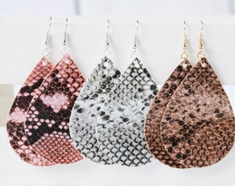 May include: Three pairs of dangle earrings with a teardrop shape. The earrings are made of faux leather with a snakeskin pattern. The earrings are in pink, gray, and brown.