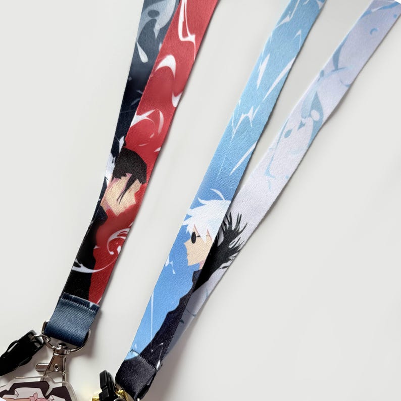 Op de afbeelding: Twee kleurrijke lanyards met geprinte anime-personages. Een lanyard is rood en blauw met een zwart-wit anime-personage. De andere lanyard is blauw en wit met een zwart-wit anime-personage.