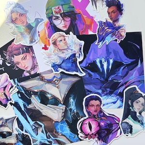 May include: A selection of character stickers with vibrant designs. The stickers depict detailed illustrations of individuals with varied hairstyles and clothing. The colour scheme includes blues, purples, and greens, with some stickers having a white border.