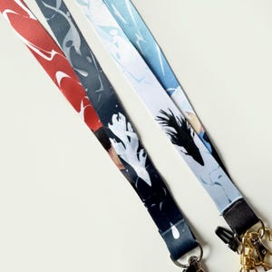 Op de afbeelding: Drie kleurrijke lanyards met zwart-witte abstracte ontwerpen. Elke lanyard heeft een zwarte draaibare clip en een gouden metalen sluiting.