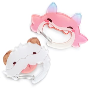 Op de afbeelding: Twee cartoon-stijl karabijnhaakclips. Eén is roze met een vossendesign, de andere is wit met een berenontwerp. Beide hebben zilveren metalen clips. De vosclip heeft blauwe en roze gradiëntoren. De beerclip heeft bruine oren.