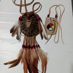 May include: Handmade Native American-style pendant and pouch set. The pendant features a turtle shell base, adorned with feathers, beads, and leather. The pouch is tan leather with a beaded design. The set is crafted with natural materials and intricate details.