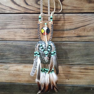May include: A handcrafted Native American-style pendant necklace. The pendant features a leather backing with beadwork in black, red, yellow, and white. It is adorned with feathers and beads in shades of green, brown, and white, suspended from a braided leather cord.