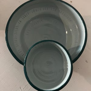May include: A large and a small round ceramic bowl with a glossy light gray interior and a dark green rim. The larger bowl features embossed text along the inner wall that reads, "THEY BROKE BREAD IN THEIR HOMES AND ATE TOGETHER WITH SINCERE HEARTS."