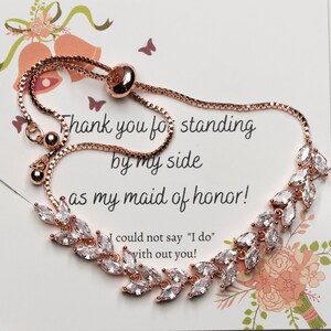May include: Rose gold bridesmaid bracelet with a delicate chain and clear crystal leaves. The bracelet has a pull-tie closure and a card that reads "Thank you for standing by my side as my maid of honor! I could not say "I do" with out you!"