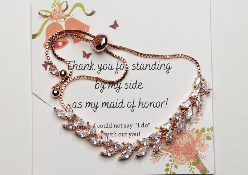 May include: Rose gold bridesmaid bracelet with a delicate chain and clear crystal leaves. The bracelet has a pull-tie closure and a card that reads "Thank you for standing by my side as my maid of honor! I could not say "I do" with out you!"