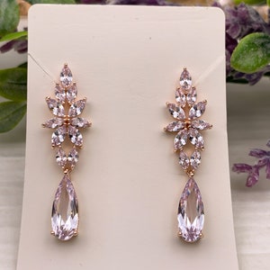 May include: A pair of rose gold dangle earrings with pink crystal teardrop and flower accents.