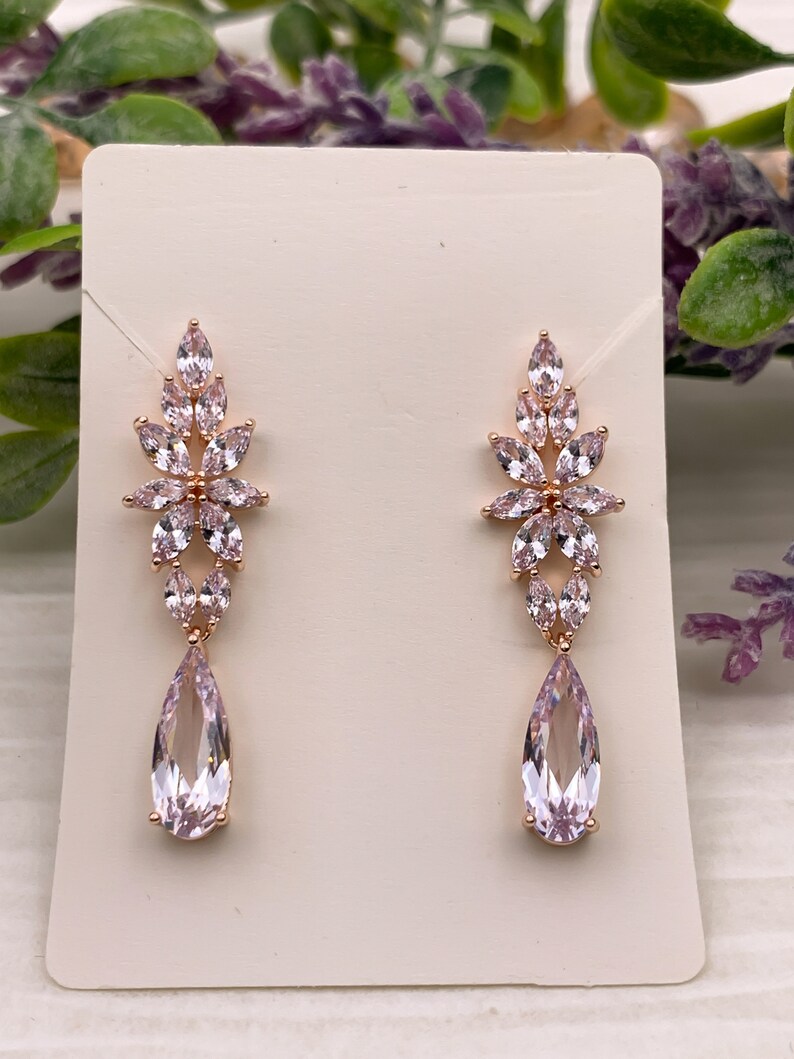 May include: A pair of rose gold dangle earrings with pink crystal teardrop and flower accents.
