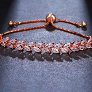 May include: A rose gold adjustable bracelet with a delicate chain and a row of clear cubic zirconia stones set in a leaf design.