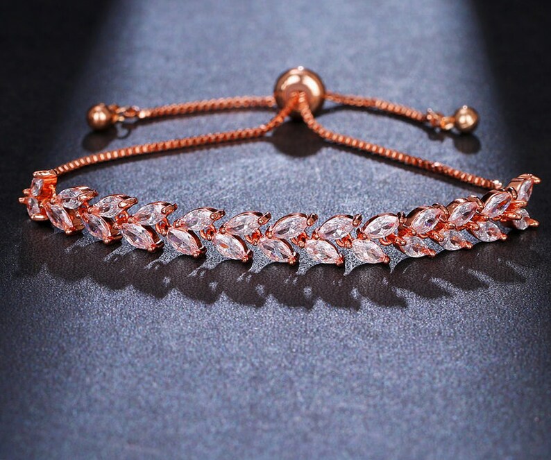 May include: A rose gold adjustable bracelet with a delicate chain and a row of clear cubic zirconia stones set in a leaf design.