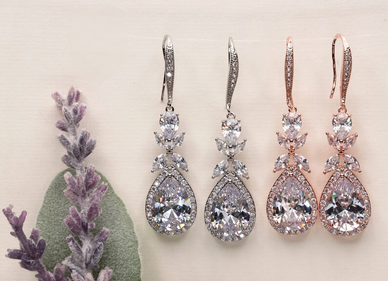 May include: Three pairs of teardrop-shaped dangle earrings with crystal accents. The earrings are available in silver, rose gold, and gold finishes.