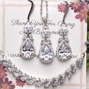 May include: A silver bridal jewelry set with a teardrop pendant necklace and matching earrings. The necklace and earrings feature a pear-shaped crystal surrounded by smaller crystals in a floral design.