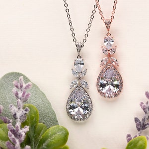 May include: Two teardrop-shaped crystal necklaces with silver and rose gold chains. The pendants feature a large teardrop crystal surrounded by smaller crystals.