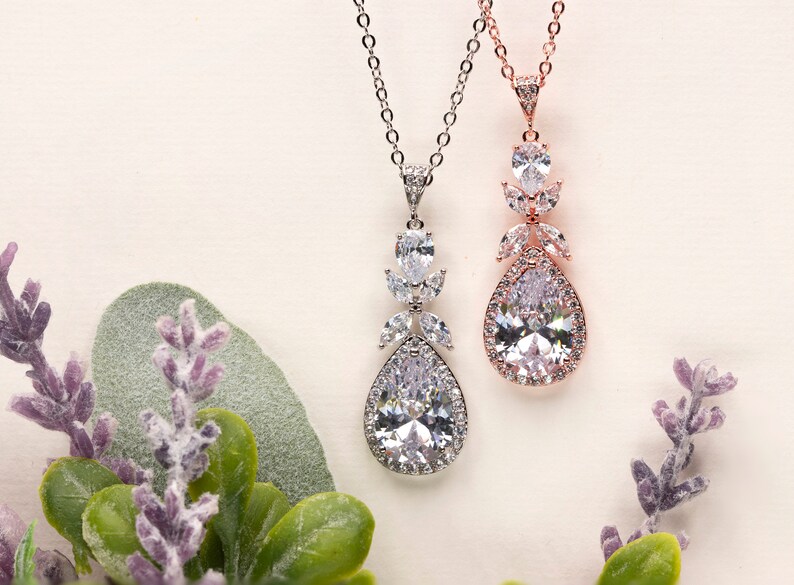 May include: Two teardrop-shaped crystal necklaces with silver and rose gold chains. The pendants feature a large teardrop crystal surrounded by smaller crystals.