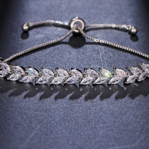May include: A silver adjustable bracelet with a delicate chain and a row of sparkling clear cubic zirconia stones set in a leaf design.