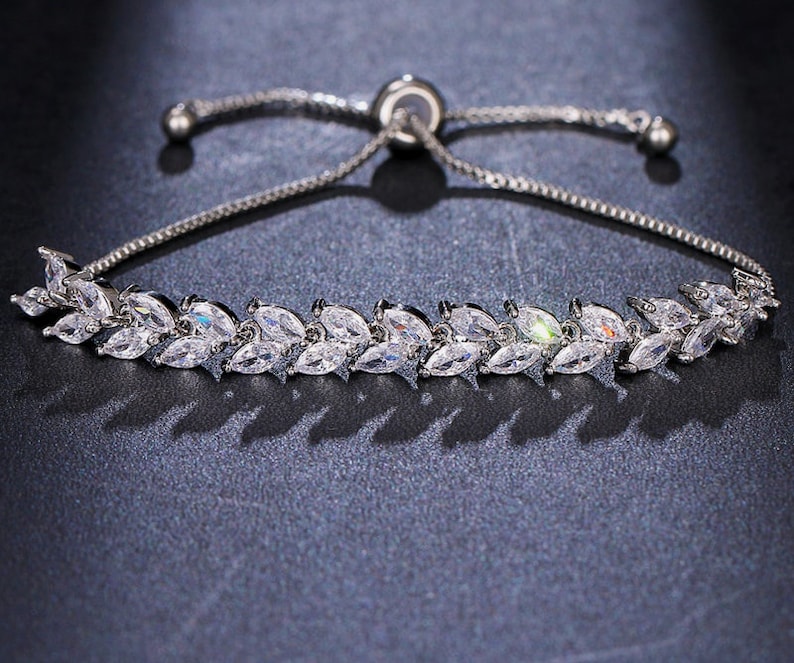 May include: A silver adjustable bracelet with a delicate chain and a row of sparkling clear cubic zirconia stones set in a leaf design.