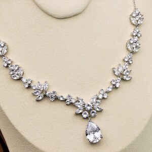 May include: A silver necklace with a teardrop-shaped pendant and a floral design. The necklace is made of clear cubic zirconia stones.