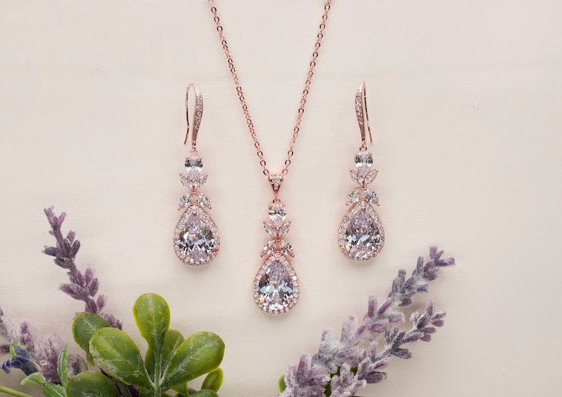 May include: A rose gold bridal jewelry set with a teardrop pendant necklace and matching earrings. The set features clear cubic zirconia stones.