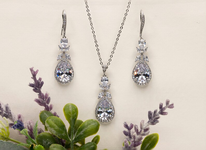 May include: A silver bridal jewelry set with a teardrop pendant necklace and matching earrings. The set features clear cubic zirconia stones.