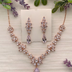 May include: A rose gold bridal necklace and earrings set with a pear-shaped crystal pendant and floral accents.