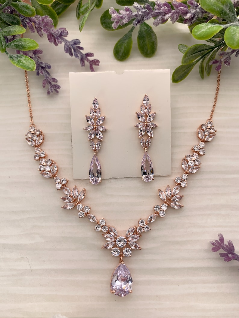 May include: A rose gold bridal necklace and earrings set with a pear-shaped crystal pendant and floral accents.