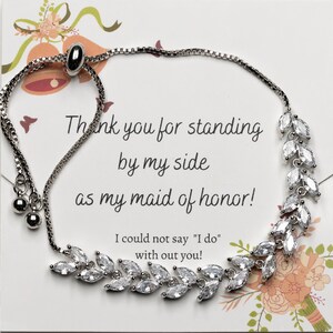 May include: A silver bracelet with a delicate chain and a charm featuring a cluster of clear rhinestones. The bracelet has a pull-string closure. The card reads "Thank you for standing by my side as my maid of honor! I could not say "I do" with out you!"