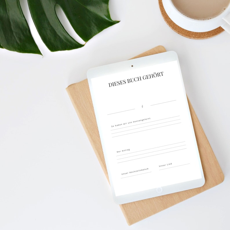 May include: A white tablet with a brown cover on a white surface. The tablet has a blank form with the text "Dieses Buch geh&ouml;rt" at the top. The form has lines for filling in information such as "So haben wir uns kennengelernt", "Der Antrag", "Unser Hochzeitstag", and "Unser Lied".