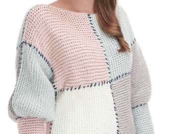 Könnte beinhalten: Ein gestrickter Pullover mit Patchwork-Muster in Rosa-, Blau- und Weißtönen. Der Pullover hat einen runden Halsausschnitt und lange Ärmel. Die Ärmel sind an den Schultern bauschig. Der Pullover ist mit einer strukturierten Masche gestrickt.