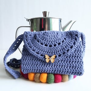 May include: A crocheted blue purse with a wooden butterfly embellishment. The purse is sitting on a colorful felt coaster.  Printable PDF Crochet Pattern.