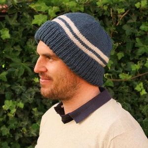 May include: A blue knit beanie with two white stripes. The beanie is worn by a person with a beard.