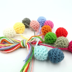 K&ouml;nnte beinhalten: Eine Sammlung bunter geh&auml;kelter Kugeln mit passenden Garnenden. Die Kugeln sind in verschiedenen Farben, darunter Rot, Orange, Gelb, Gr&uuml;n, Blau und Pink.