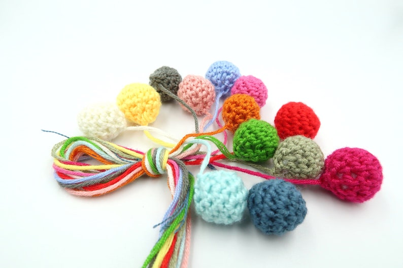 K&ouml;nnte beinhalten: Eine Sammlung bunter geh&auml;kelter Kugeln mit passenden Garnenden. Die Kugeln sind in verschiedenen Farben, darunter Rot, Orange, Gelb, Gr&uuml;n, Blau und Pink.