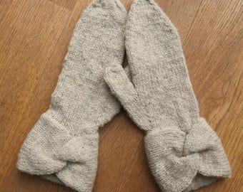 May include: A pair of beige knitted mittens with a bow detail on the cuff.