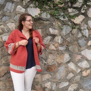 Peut inclure: Un cardigan en crochet de couleur corail avec un col ch&acirc;le et des bordures en crochet blanc sur les manches et l'ourlet.