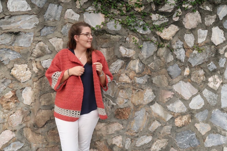 Peut inclure: Un cardigan en crochet de couleur corail avec un col ch&acirc;le et des bordures en crochet blanc sur les manches et l'ourlet.