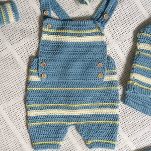 May include: A blue and white striped crocheted baby outfit with yellow accents. The outfit includes a one-piece jumpsuit with straps and a matching hat.