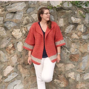 Peut inclure: Une femme portant un cardigan en crochet de couleur corail avec une bordure en crochet blanc. Le cardigan a un col ch&acirc;le et des manches trois-quarts. Elle se tient devant un mur de pierre avec des vignes vertes qui poussent dessus. Le texte "PRINTABLE PDF KNITTING PATTERN" est en haut de l'image.