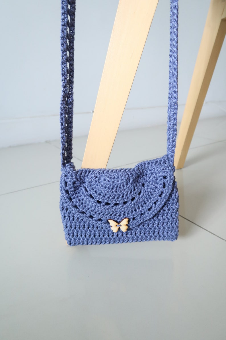 May include: A small, crocheted purse with a butterfly-shaped button. The purse is a light blue color and has a long strap.