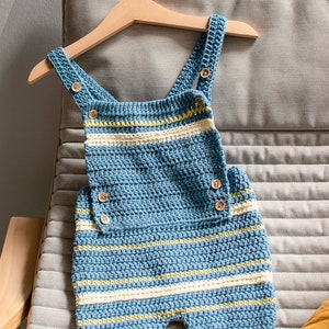 May include: A blue and white striped crocheted baby overall with wooden buttons hanging on a wooden hanger.