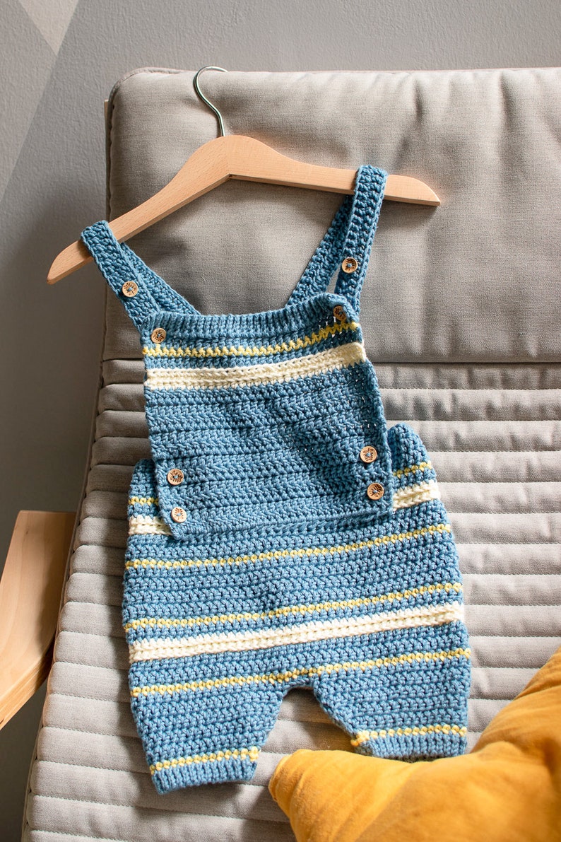 May include: A blue and white striped crocheted baby overall with wooden buttons hanging on a wooden hanger.