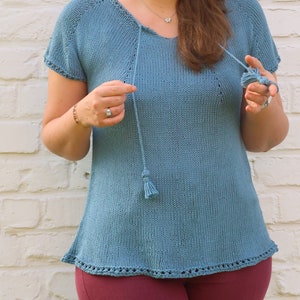 Pu&ograve; includere: Un top in maglia blu chiaro con maniche corte e scollo a V. Il top presenta un cordino con nappa e un orlo decorativo. Il top &egrave; realizzato in morbido materiale a maglia. Il top &egrave; lungo circa 61 cm.